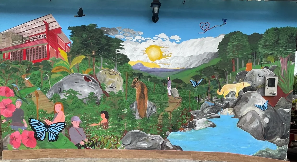 Mural de Glamorita con la casa de la finca, el sol, el río, fauna y cafetales.